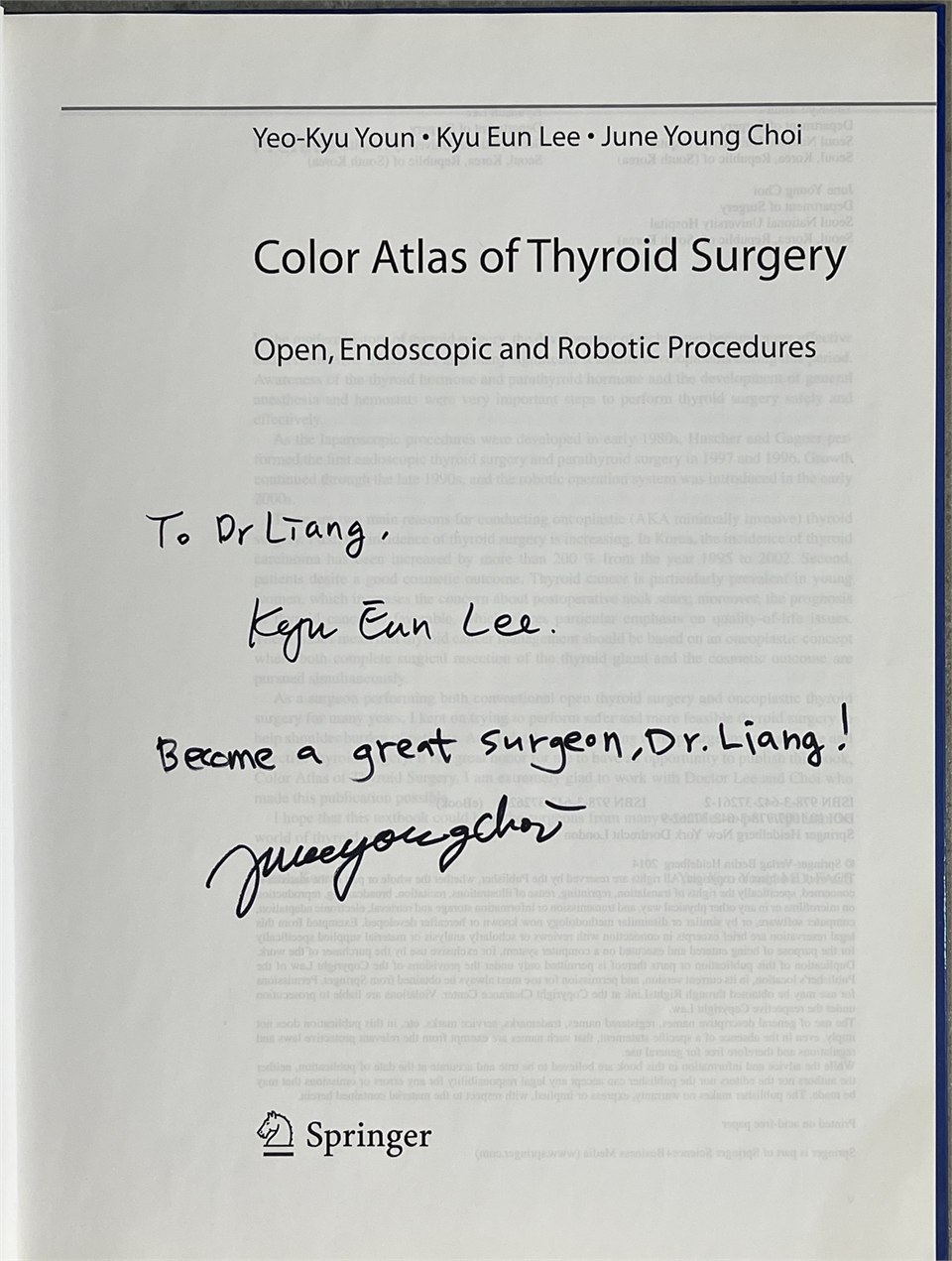 書的扉頁照片：頁面上方印著三位作者 Yeo-Kyu Youn、Kyu Eun Lee、June Young Choi，中間是書名 Color Atlas of Thyroid Surgery 與副標題 Open, Endoscopic and Robotic Procedures，頁面下方是 Springer 標誌。頁面中央有兩段黑色簽字筆的手寫字：上面一段寫 To Dr Liang. 與 Kyu Eun Lee. 的署名，下面一段寫 Become a great surgeon, Dr. Liang! 並簽上 June Young Choi