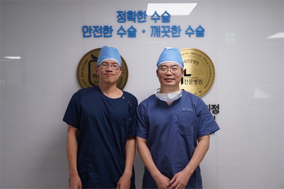 兩位戴著手術帽、穿刷手服的男醫師並肩站在白牆前合影，牆上有韓文標語與兩面金色的認證牌