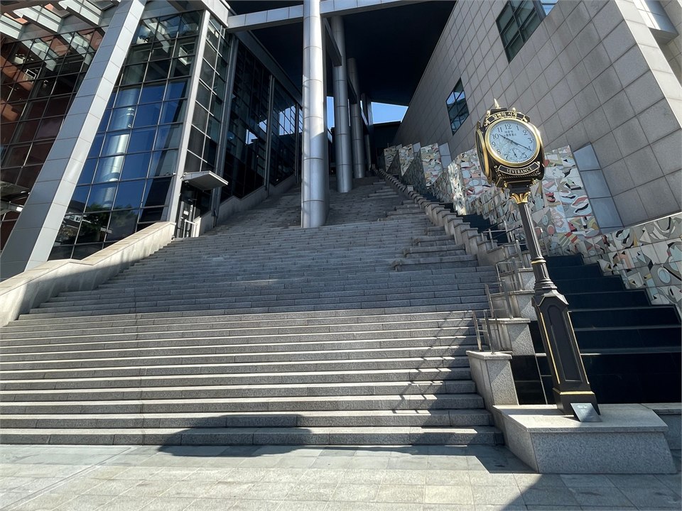 主樓入口的長階梯，右側立著一座金色的古典立鐘，鐘面下緣刻著 SEVERANCE