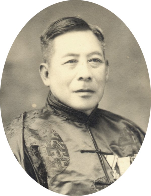 一位年長男性的黑白半身肖像照，短髮、面向鏡頭，穿著繡有暗紋的絲質長袍馬褂，胸前別著兩枚勳章